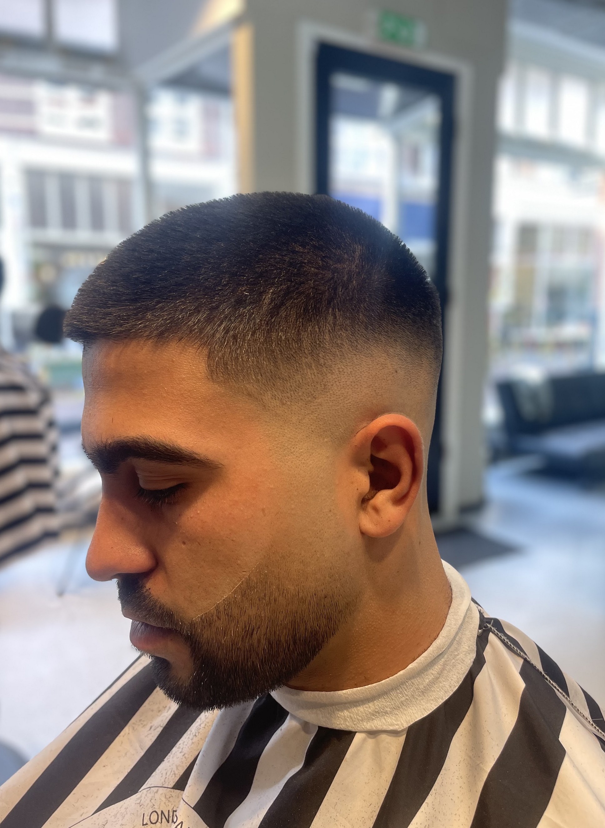 Skin fade met verzorgde baard, van opzij gezien, in een gestreepte kapmantel